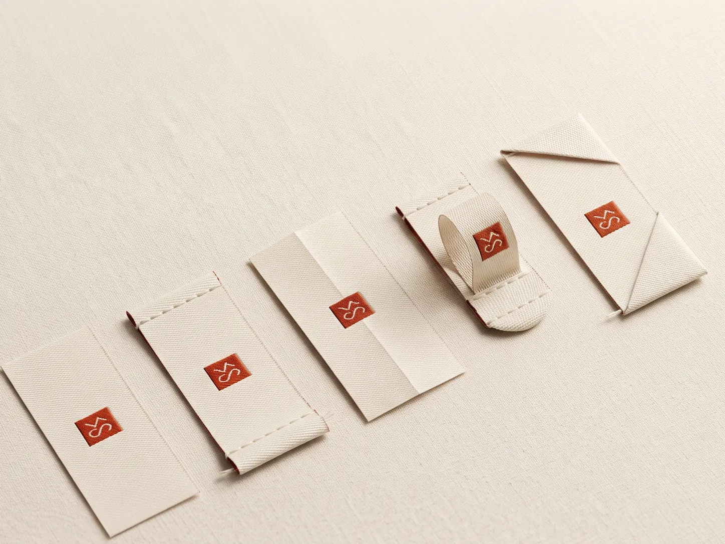 Five clothing label fold types shown side by side: straight-cut, end-fold, centre-fold, loop-fold and mitre-fold woven labels, each with a small terracotta logo