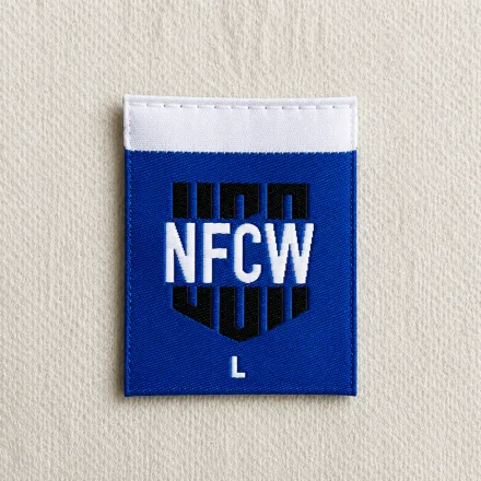 NFCW blue shield-shaped woven brand label with white wordmark, L size marker and white tab top, sportswear and uniform woven label sample