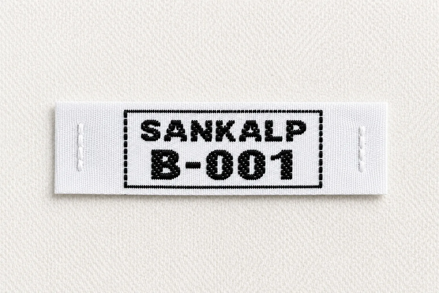 Sankalp B-001 white woven name and number label with bold black framed identifier — uniform identification woven label sample