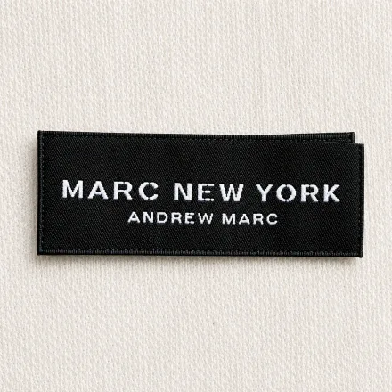 Black satin printed brand label sample with minimal white serif wordmark and secondary tagline: luxury menswear design reference, satin print finish