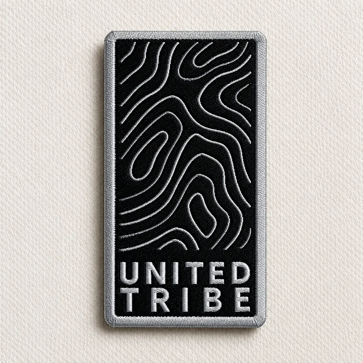 United Tribe black woven brand patch with topographic contour pattern and silver wordmark and border — outdoor and streetwear brand woven patch sample