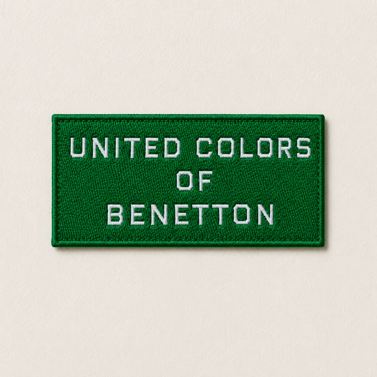 Green woven brand patch sample with white block-letter wordmark — premium casual-wear design reference, woven patch finish