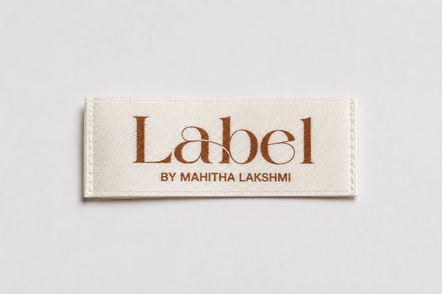 Label by Mahitha Lakshmi cream satin printed brand label with elegant copper-tone serif wordmark and tagline — boutique fashion satin printed label sample