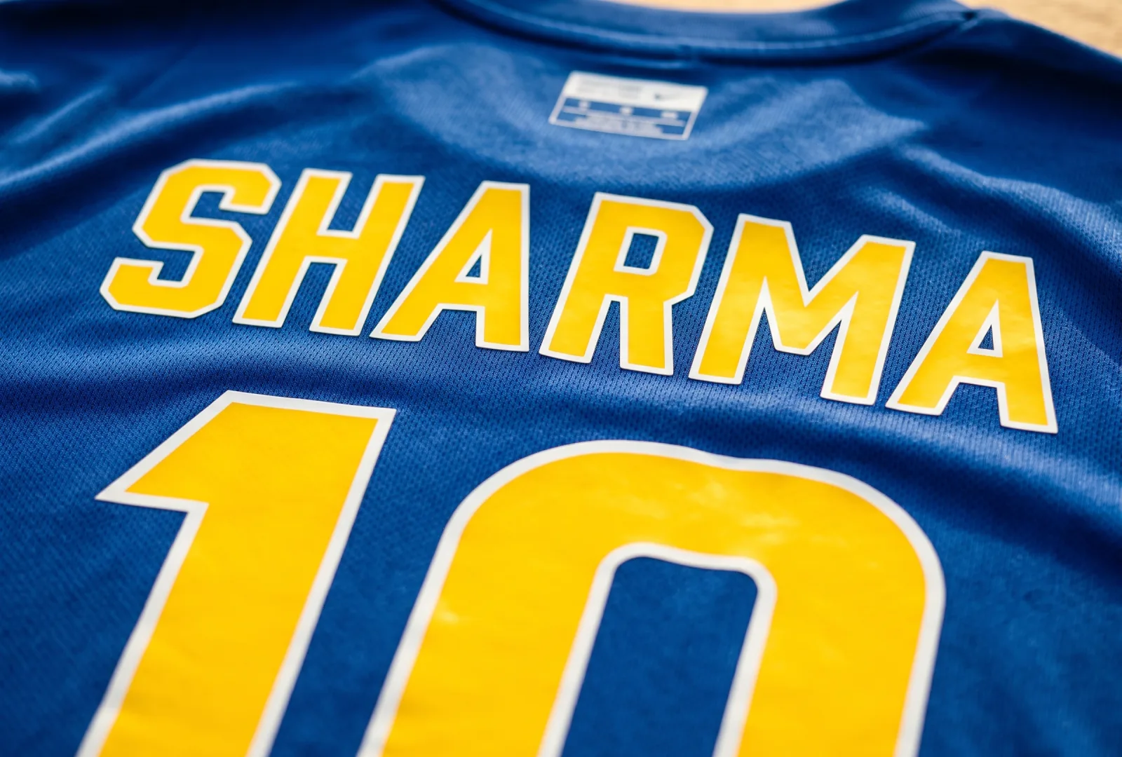 Back of a blue sports jersey with yellow heat-pressed SHARMA name and number 10 — example of sublimation and heat-press numbering for team jerseys and sportswear brands